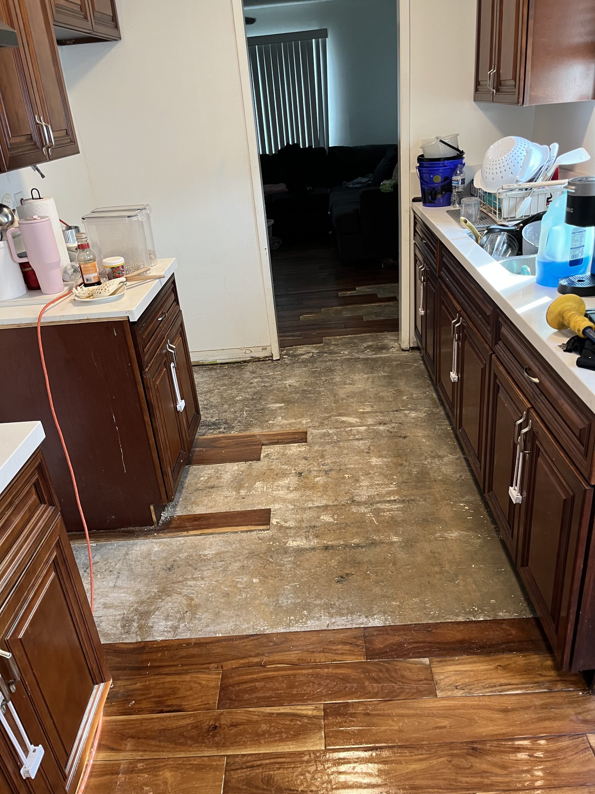 Kitchen floor before repair with damaged planks removed and bare subfloor exposed