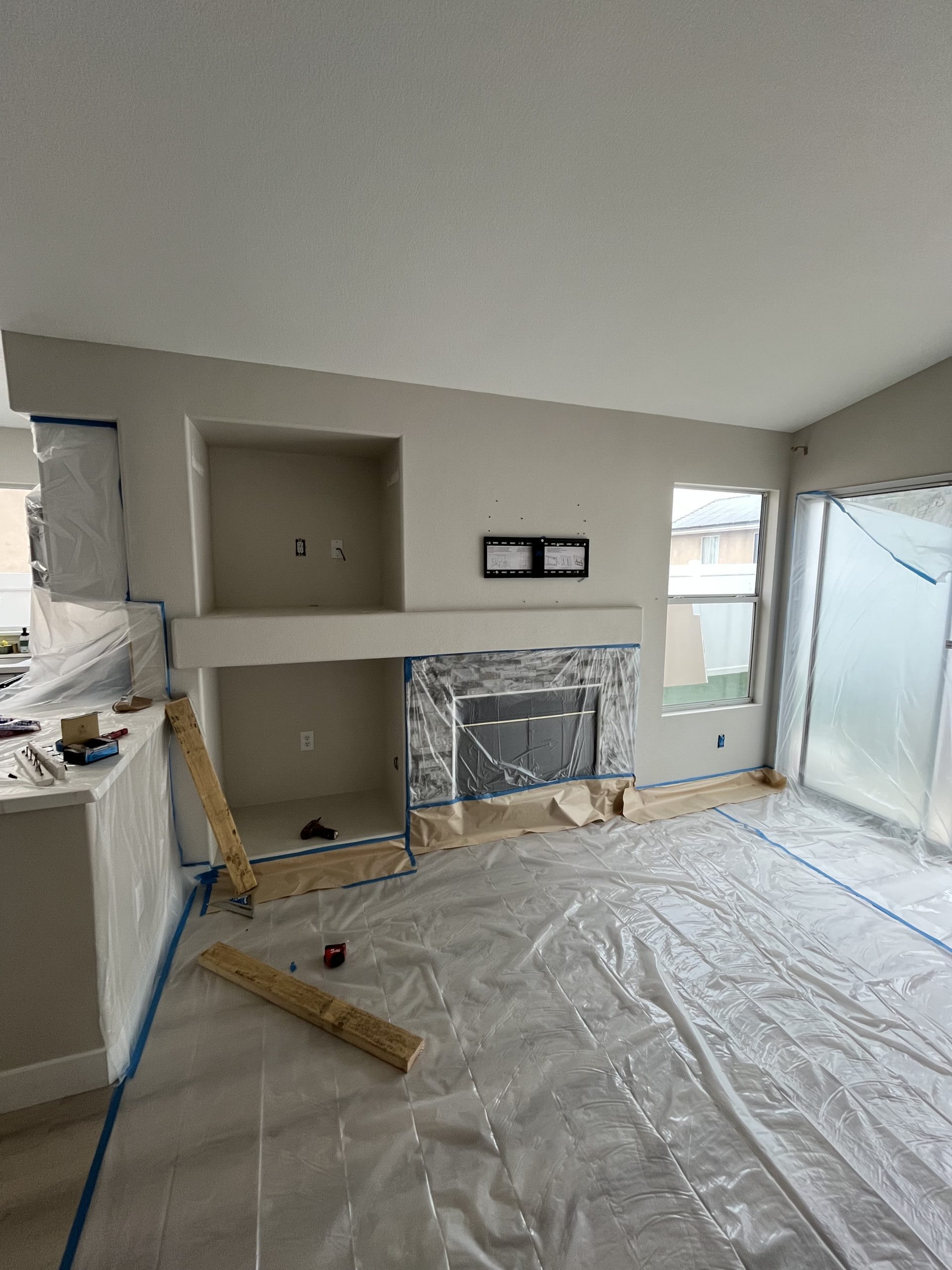 Living room during prep with floors and fireplace covered in plastic and a TV bracket on the wall